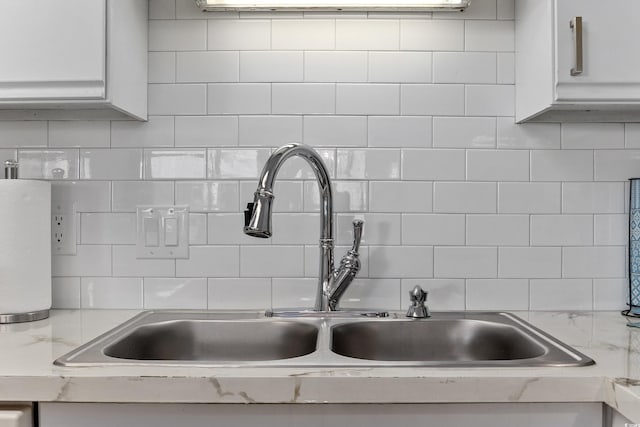 interior details with light stone counters, white cabinetry, a sink, and decorative backsplash