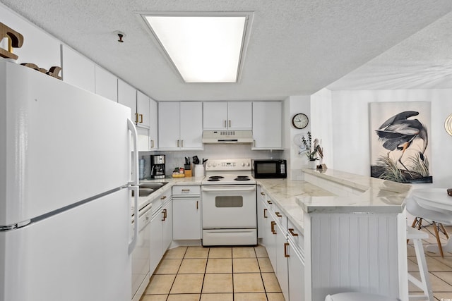 kitchen with a peninsula, white appliances, white cabinets, and under cabinet range hood