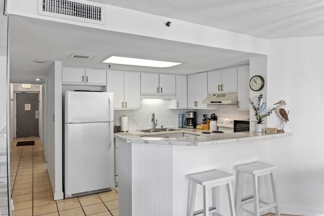 kitchen with visible vents, freestanding refrigerator, a peninsula, under cabinet range hood, and a sink