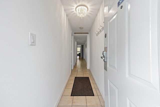 hall with light tile patterned floors, a textured ceiling, visible vents, and baseboards