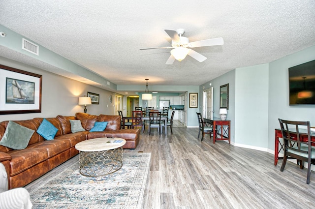 living room with wood-type flooring, ceiling fan, and a textured ceiling