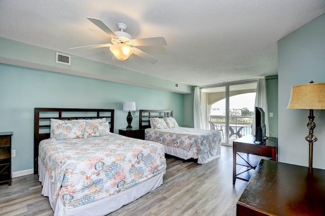 bedroom with expansive windows, access to outside, ceiling fan, a textured ceiling, and light hardwood / wood-style flooring