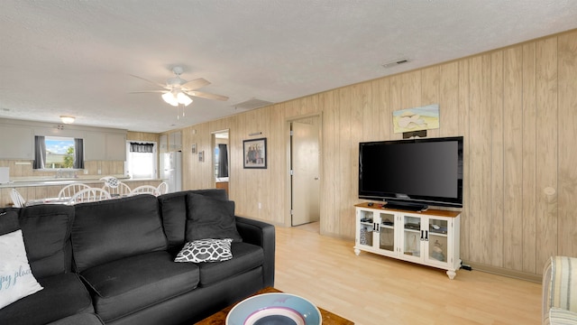 living room with a textured ceiling, wood walls, light hardwood / wood-style flooring, and ceiling fan