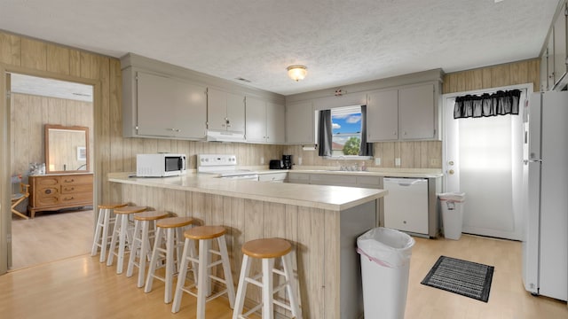 kitchen with light wood-type flooring, kitchen peninsula, white appliances, and a breakfast bar