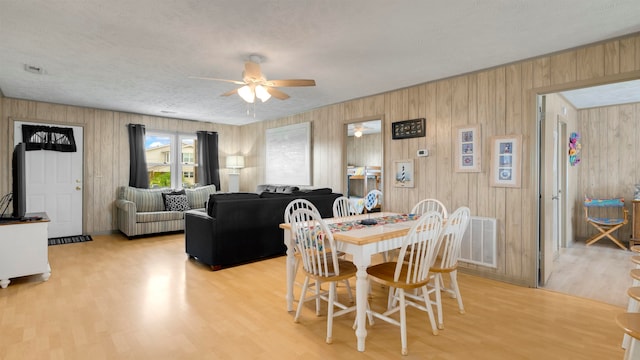 dining area featuring wood walls, a textured ceiling, light hardwood / wood-style flooring, and ceiling fan