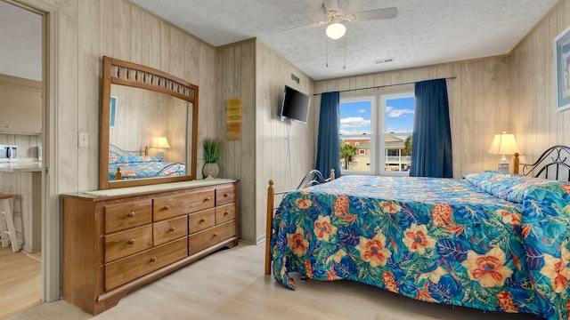 bedroom with wooden walls, a textured ceiling, ceiling fan, and light wood-type flooring