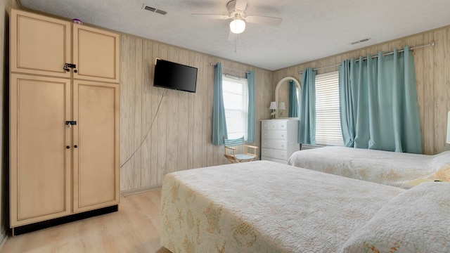 bedroom with light hardwood / wood-style flooring, a textured ceiling, ceiling fan, and wooden walls