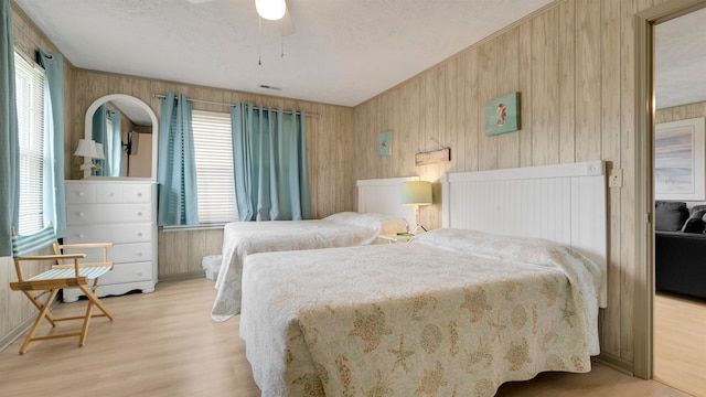 bedroom featuring wood walls, light hardwood / wood-style flooring, and multiple windows