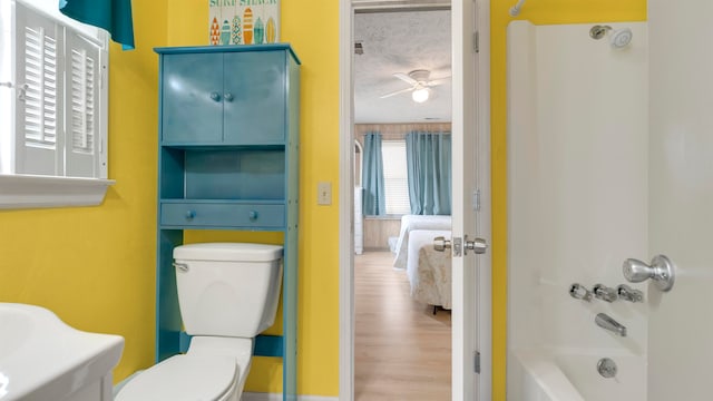 bathroom with ceiling fan, hardwood / wood-style floors, shower / tub combination, toilet, and a textured ceiling