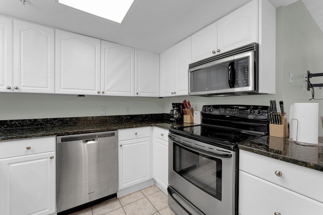 kitchen featuring appliances with stainless steel finishes, white cabinets, dark stone countertops, and light tile patterned floors