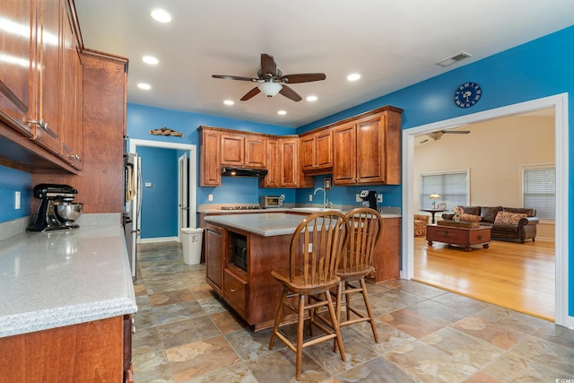 kitchen with light stone counters, sink, a breakfast bar, and ceiling fan