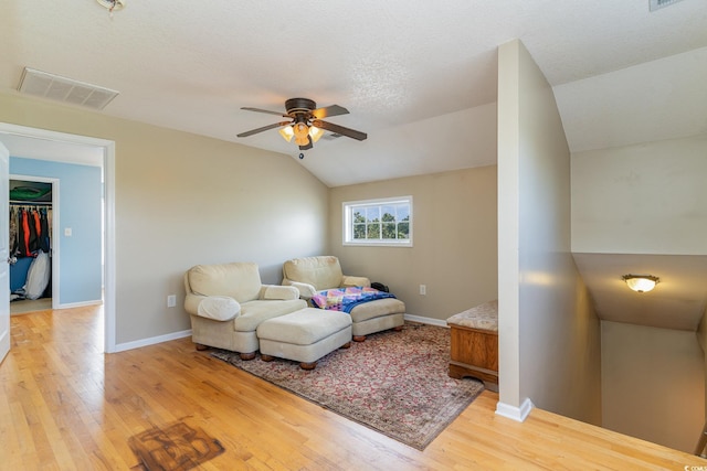 living room with ceiling fan, lofted ceiling, wood-type flooring, and a textured ceiling