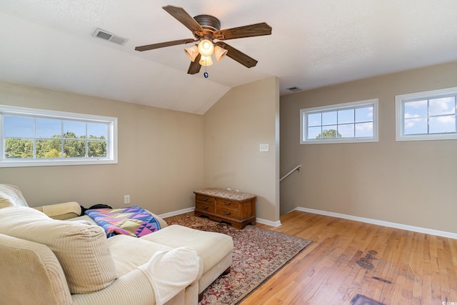 living area with ceiling fan, vaulted ceiling, light hardwood / wood-style flooring, and a textured ceiling