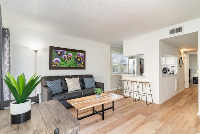 living room with ornamental molding, visible vents, light wood-style flooring, and a textured ceiling