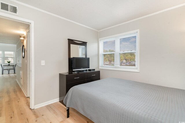 bedroom featuring multiple windows, ornamental molding, and light hardwood / wood-style floors