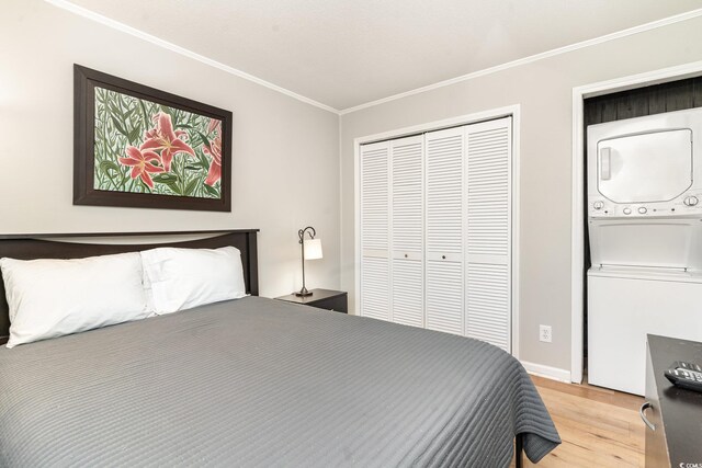 bedroom with a closet, crown molding, light hardwood / wood-style flooring, and stacked washer / drying machine