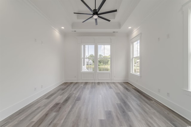 empty room featuring ceiling fan, light wood-type flooring, ornamental molding, and a tray ceiling