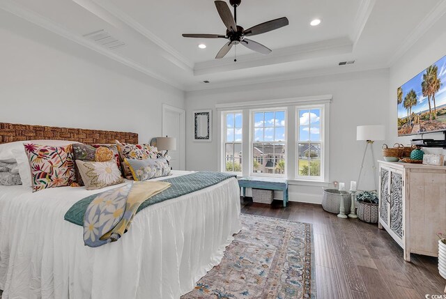 bedroom with crown molding, dark wood-type flooring, a raised ceiling, and ceiling fan