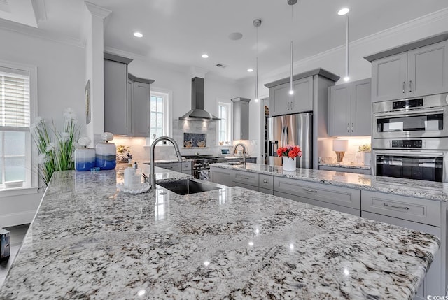 kitchen with pendant lighting, sink, appliances with stainless steel finishes, light stone counters, and wall chimney exhaust hood