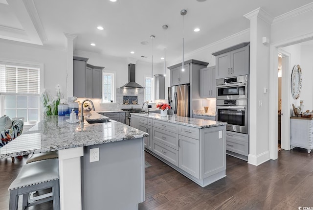 kitchen with sink, decorative light fixtures, a center island, stainless steel appliances, and wall chimney range hood