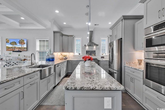 kitchen with wall chimney exhaust hood, appliances with stainless steel finishes, a center island, and gray cabinetry