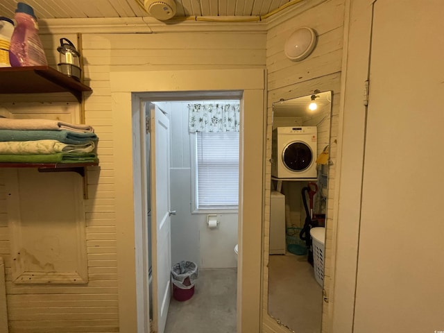 bathroom featuring wood ceiling, stacked washer / drying machine, concrete flooring, wood walls, and toilet