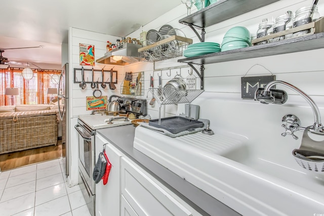 kitchen featuring light tile patterned floors, white cabinetry, stainless steel range with electric cooktop, and sink