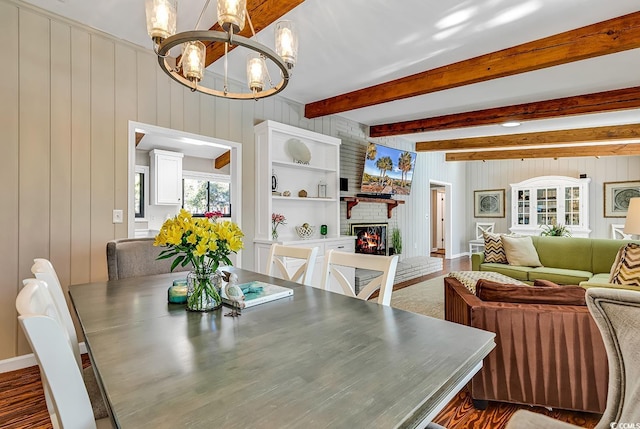 dining area featuring a chandelier, wood walls, built in shelves, beam ceiling, and a fireplace