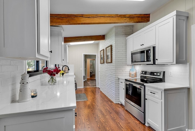 kitchen with appliances with stainless steel finishes, vaulted ceiling with beams, light stone countertops, dark hardwood / wood-style flooring, and white cabinetry