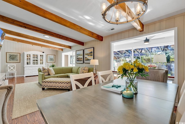 dining space with ceiling fan with notable chandelier, hardwood / wood-style flooring, and beam ceiling