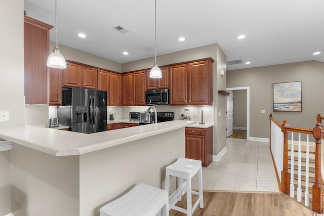 kitchen with a kitchen breakfast bar, pendant lighting, backsplash, light hardwood / wood-style floors, and black fridge