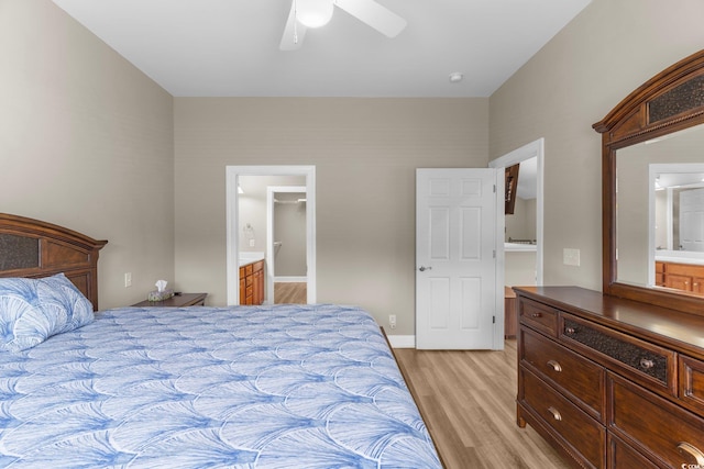 bedroom featuring light hardwood / wood-style flooring, connected bathroom, ceiling fan, and a walk in closet