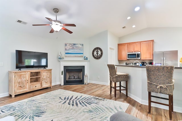 living room with ceiling fan, light hardwood / wood-style flooring, and vaulted ceiling