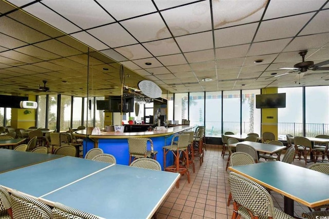 tiled dining space featuring ceiling fan, a drop ceiling, and floor to ceiling windows