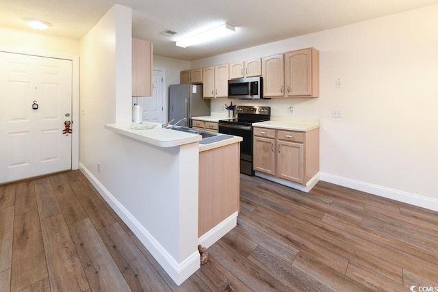 kitchen with a sink, stainless steel appliances, light countertops, and light brown cabinetry