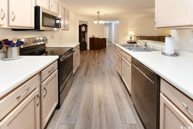 kitchen featuring light brown cabinets, a chandelier, light wood-type flooring, stainless steel appliances, and sink