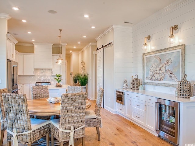 dining area featuring a barn door, beverage cooler, light hardwood / wood-style floors, and crown molding