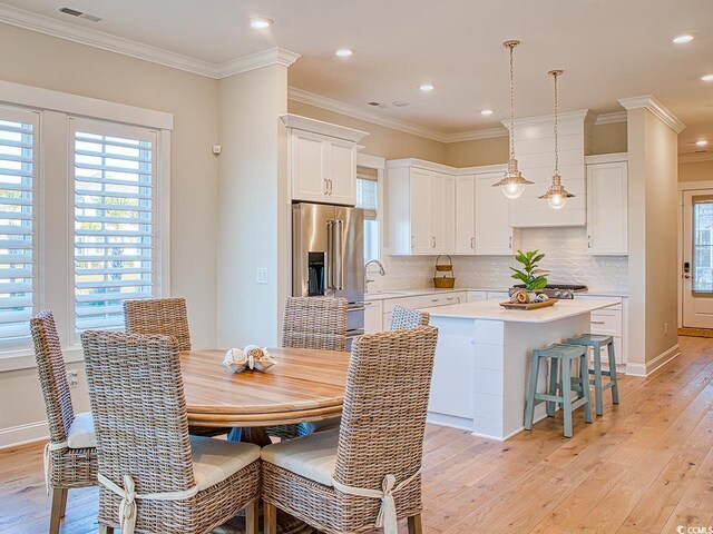 dining space featuring sink, light wood-type flooring, and ornamental molding