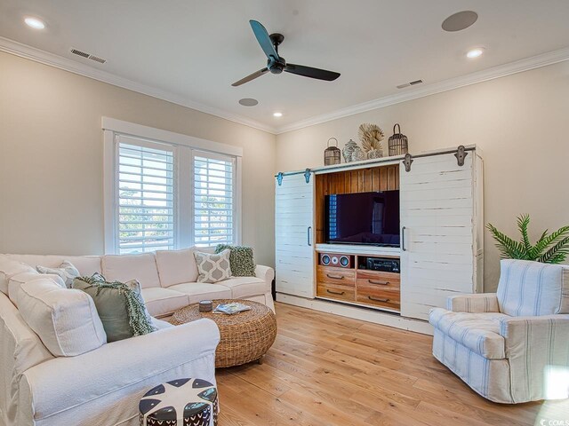 living room featuring ceiling fan, crown molding, a barn door, and light hardwood / wood-style floors