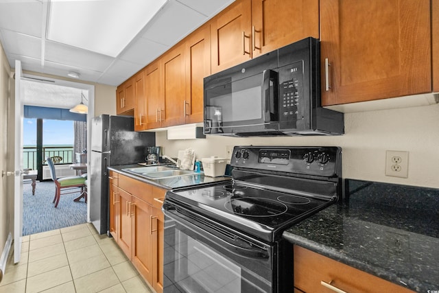 kitchen featuring light tile patterned flooring, sink, a drop ceiling, black appliances, and dark stone countertops