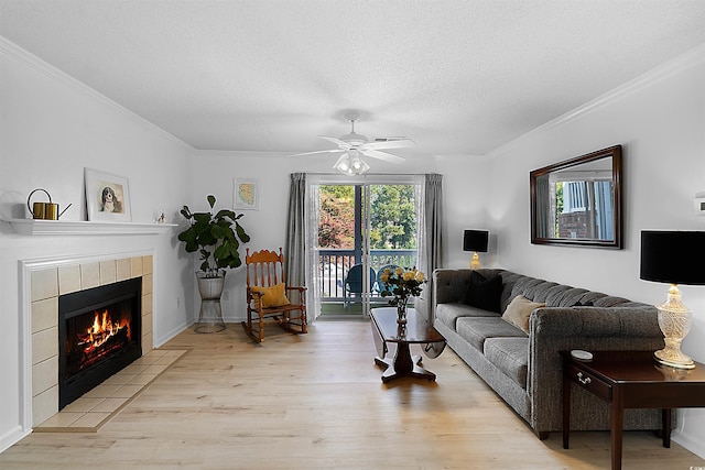 living room with a textured ceiling, light wood-type flooring, ceiling fan, a tile fireplace, and crown molding