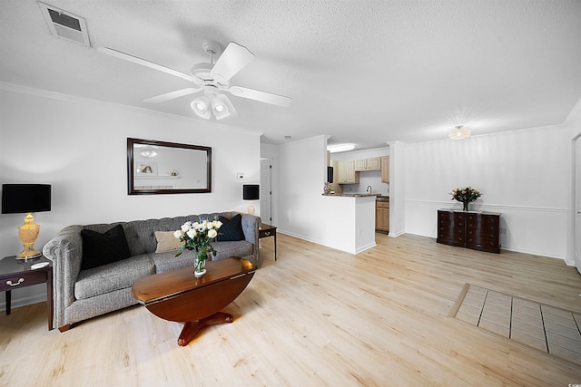 living room with light wood-type flooring, a textured ceiling, ceiling fan, and ornamental molding