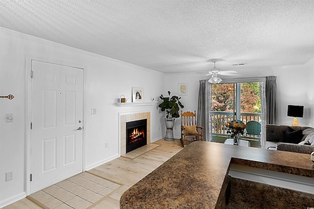 living room with a textured ceiling, light hardwood / wood-style floors, ceiling fan, crown molding, and a tiled fireplace