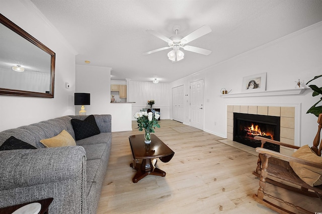 living room featuring a textured ceiling, ornamental molding, light wood-type flooring, ceiling fan, and a tile fireplace