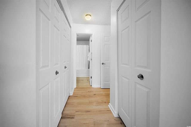 corridor featuring light wood-type flooring and a textured ceiling