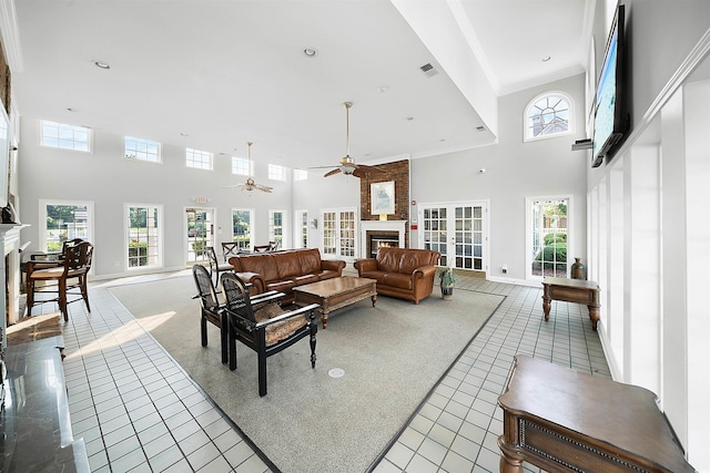 living room with ceiling fan, a towering ceiling, light tile patterned floors, a fireplace, and ornamental molding