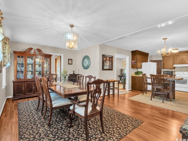 dining area with a textured ceiling, light hardwood / wood-style floors, and a chandelier