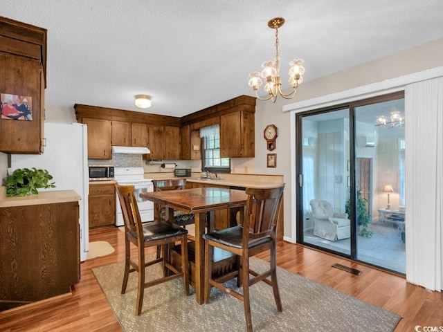 dining space with a textured ceiling, a notable chandelier, and light wood-type flooring