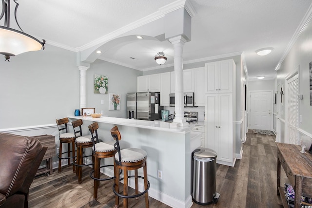 kitchen with appliances with stainless steel finishes, white cabinetry, decorative columns, and kitchen peninsula