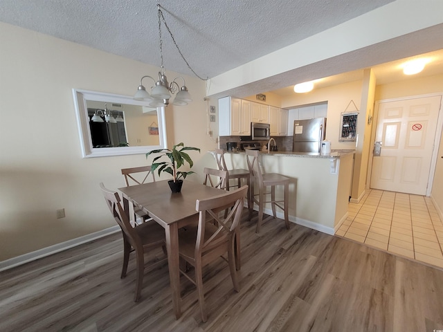 dining space with an inviting chandelier, light hardwood / wood-style floors, sink, and a textured ceiling